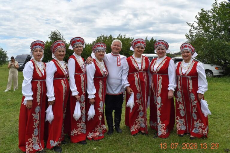 Фотография ансамбля "Заряночка". Девушки в красных народных костюмах, по центру стоит гармонист