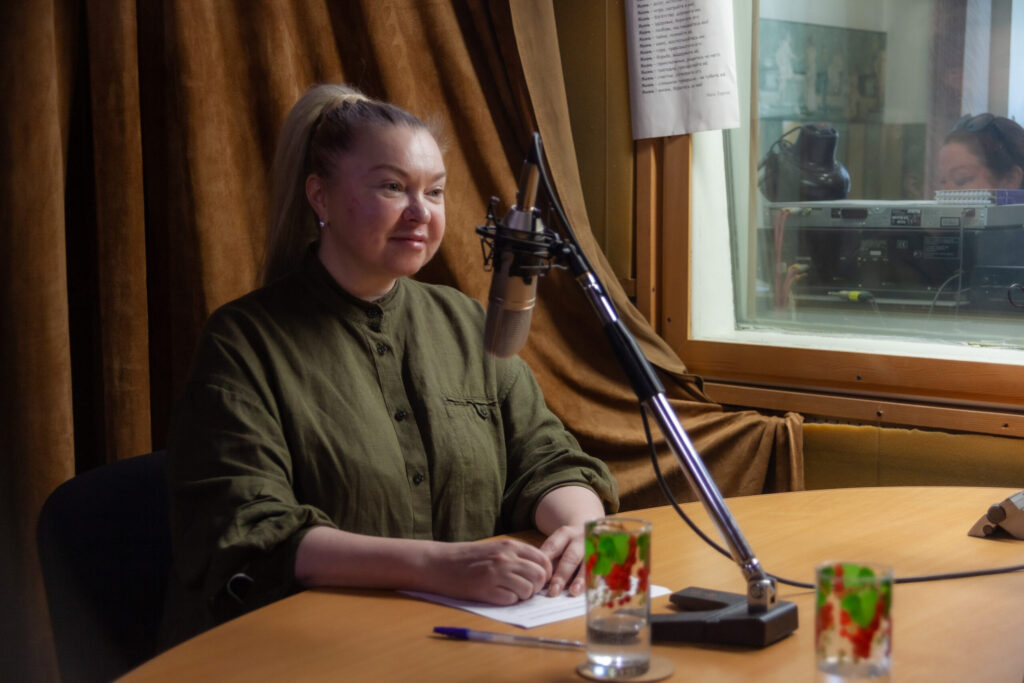 Мария Самсонова, заместитель директора. Сидит за столом в студии звукозапись, на столе стоит микрофон. Записывается передача "Мир равных возможностей"